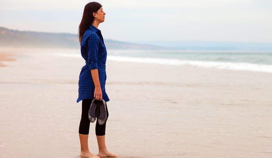 Femme seule face à la mer, en pleine réflexion : Et si le but n’était pas d’avoir plus… mais d’arrêter de vouloir plaire ?